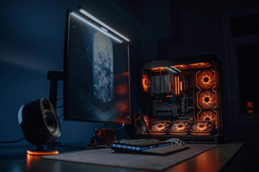 A futuristic-looking black gaming PC sits on a desktop, with an exposed tower lit up by orange LED lights